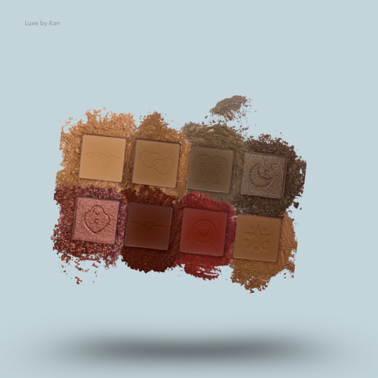 Eight neutral-toned eyeshadows with embossed date night themed designs, arranged in a two-by-four grid, scattered with loose pigment.