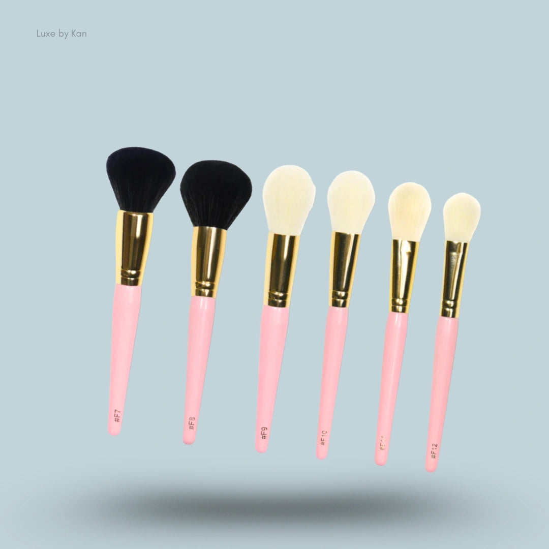 Six makeup brushes with pink handles, gold ferrules, and varying brush heads.