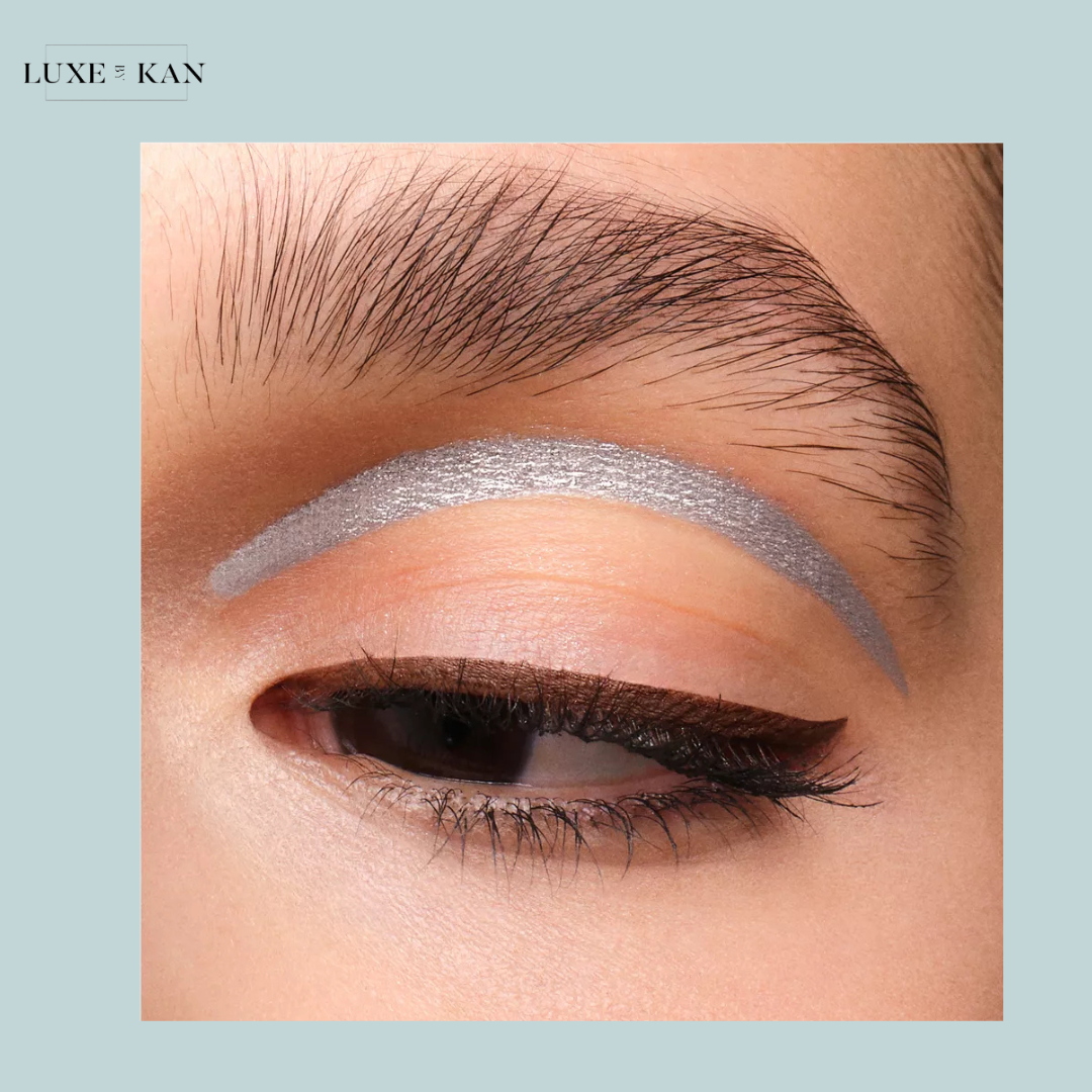 Close-up of a woman's eye showcasing bold silver eyeshadow above a subtle warm base, paired with defined eyeliner and natural brows.