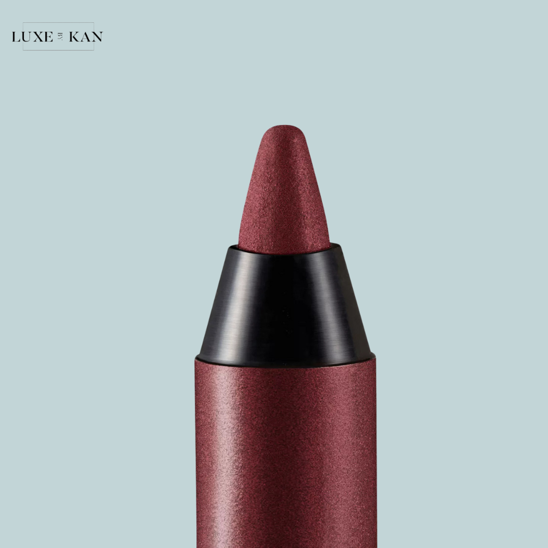 Close-up of a burgundy lipstick crayon with a pointed tip, set against a soft blue background. Brand logo: LUXE KAN.