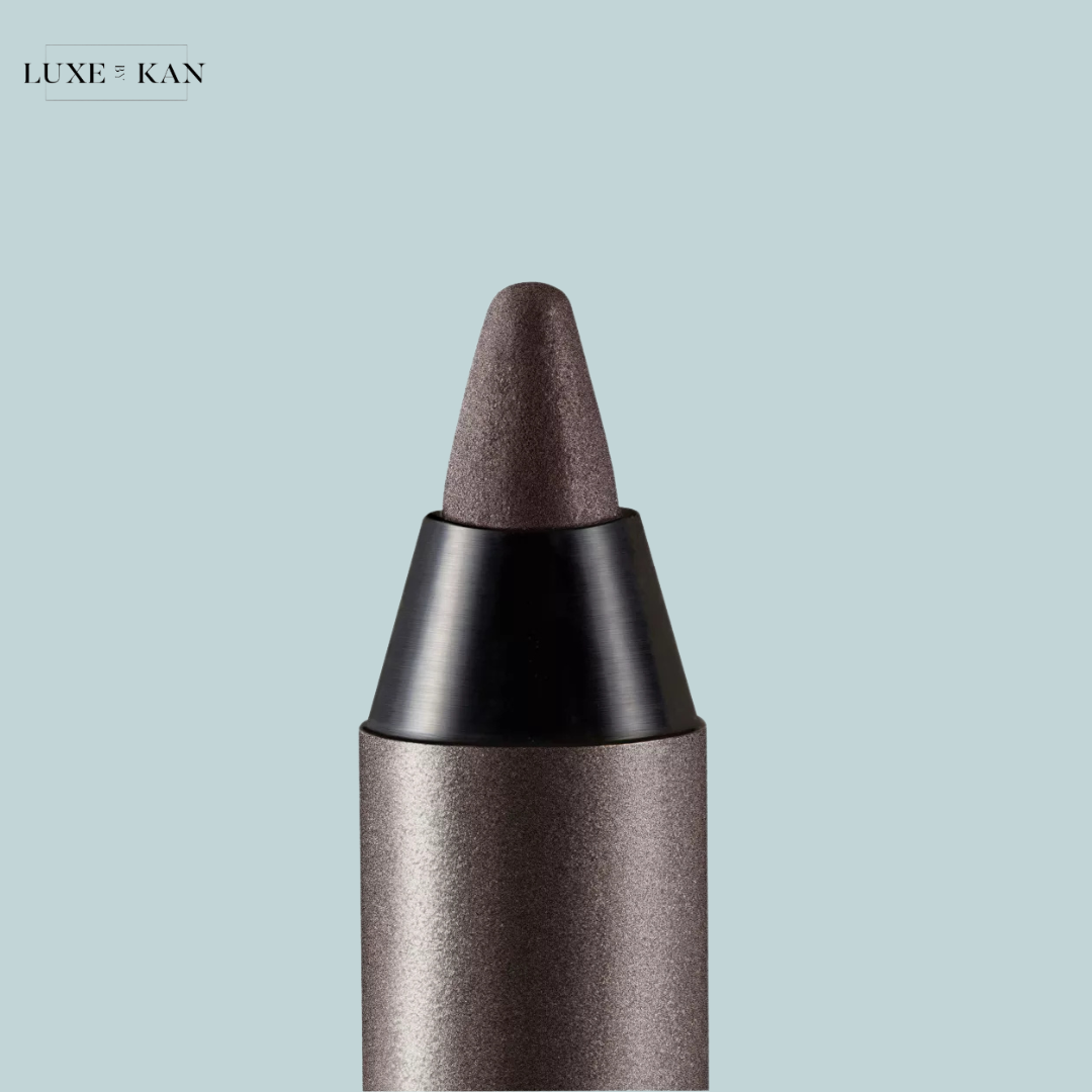 Close-up of a luxe, gray-shaped makeup crayon with a textured tip against a soft blue background. Brand: Luxe & Kan.