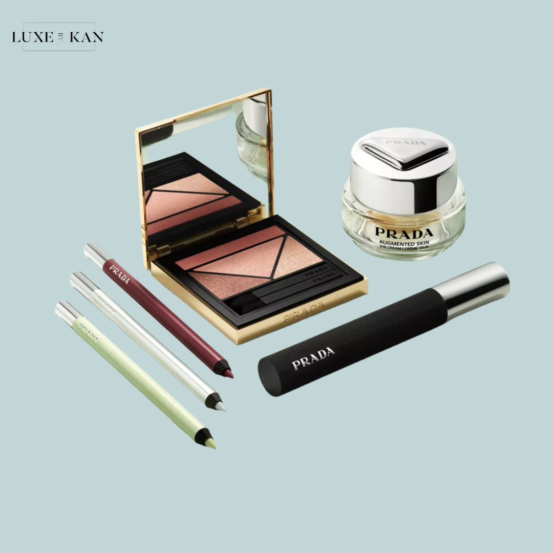 A selection of Prada makeup products, including eyeshadow, eyeliner pencils, and a skincare cream, arranged on a soft blue background.