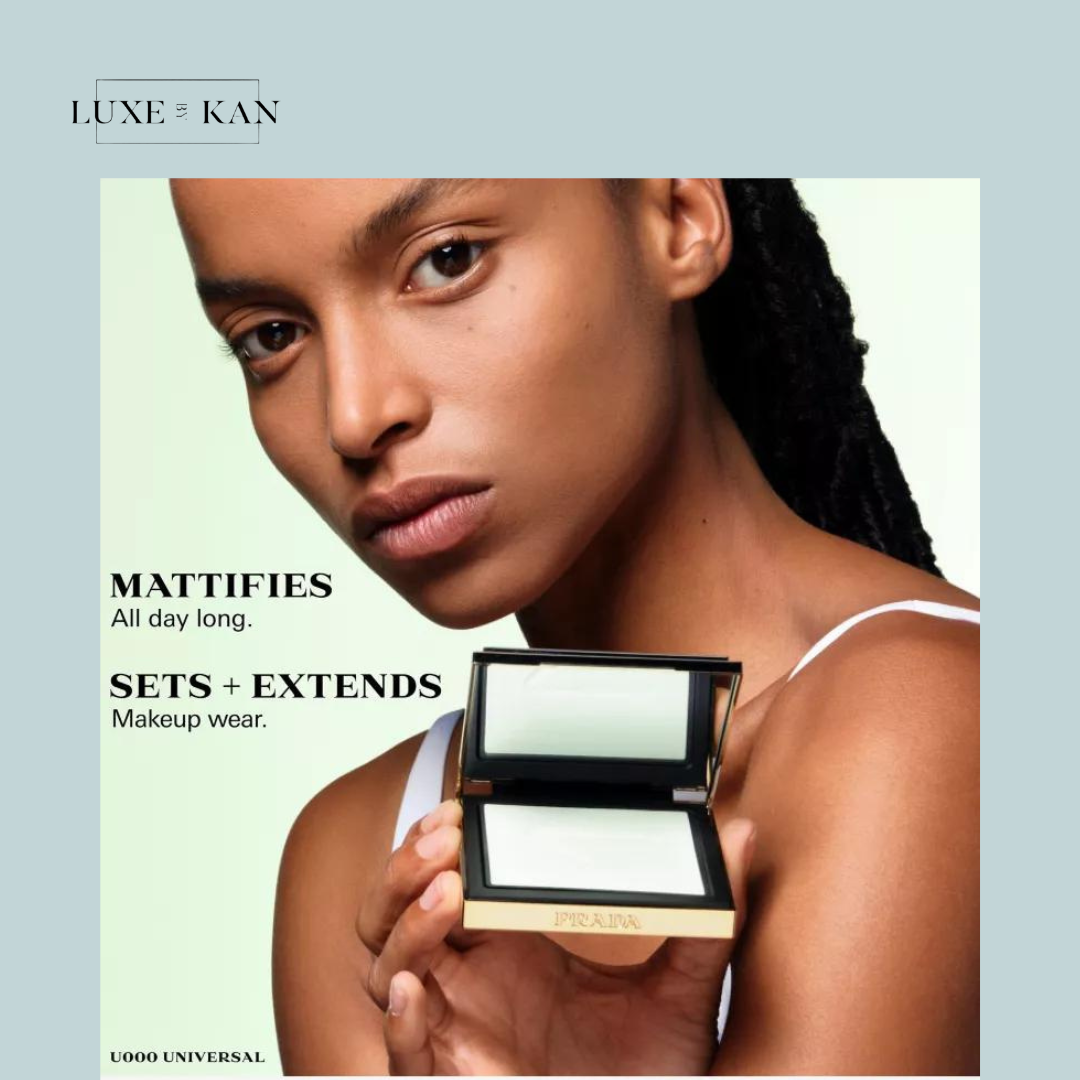 A person holds an open square prada reset rebalancing setting powder with a mirrored lid, showcasing a smooth, reflective surface, against a light green background.