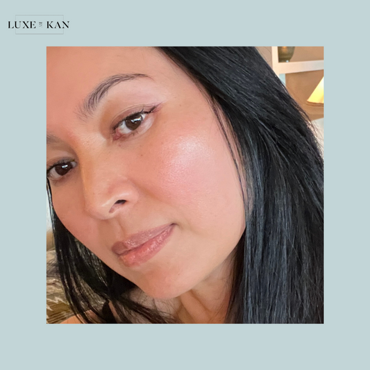 A close-up of a person with long, dark hair, against a soft, light blue background with interior decor visible in the backdrop.