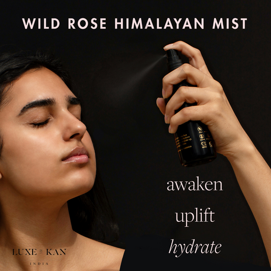 A hand sprays Wild Rose Himalayan Mist, with text highlighting its benefits: awaken, uplift, hydrate. Background is dark.