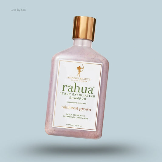 Rahua scalp exfoliating shampoo bottle, light pink color with gold cap and label, on a light blue background.