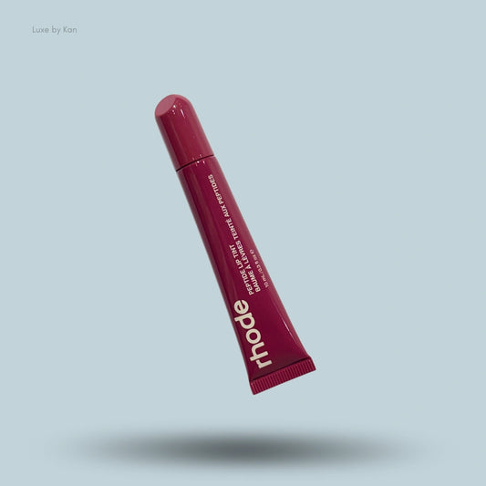 A tube of Rhode Peptide Lip Tint in a raspberry jelly shade, casting a shadow on a light blue background.
