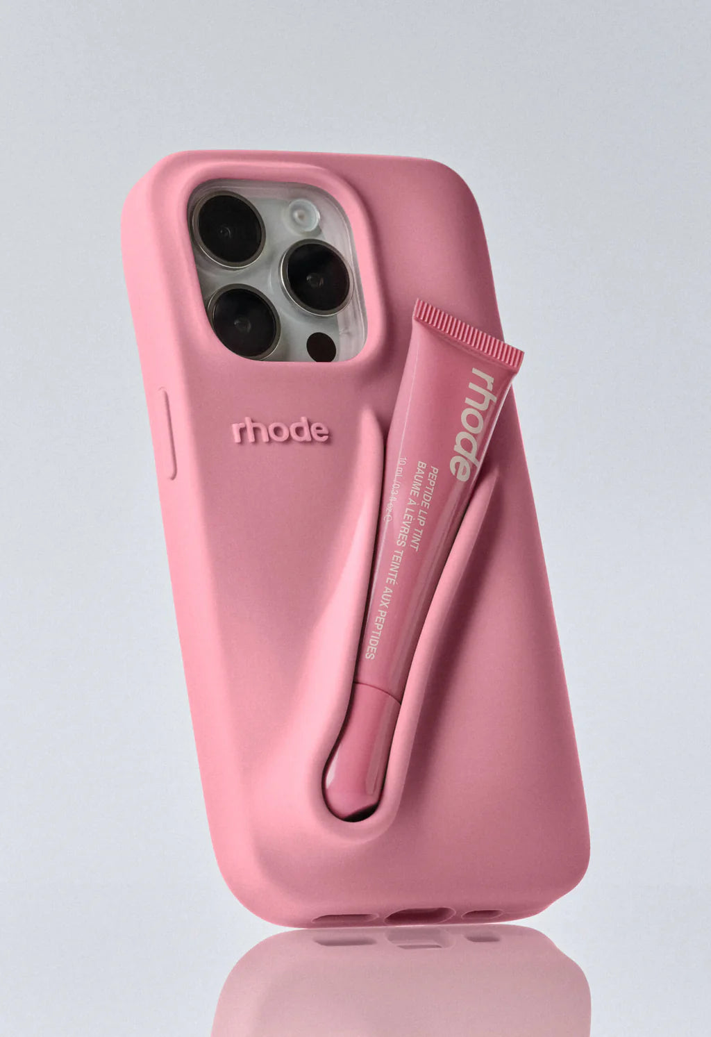 Pink Rhode phone case with the brand name embossed on the side, featuring a pink lip tint tube in a slot on the back.