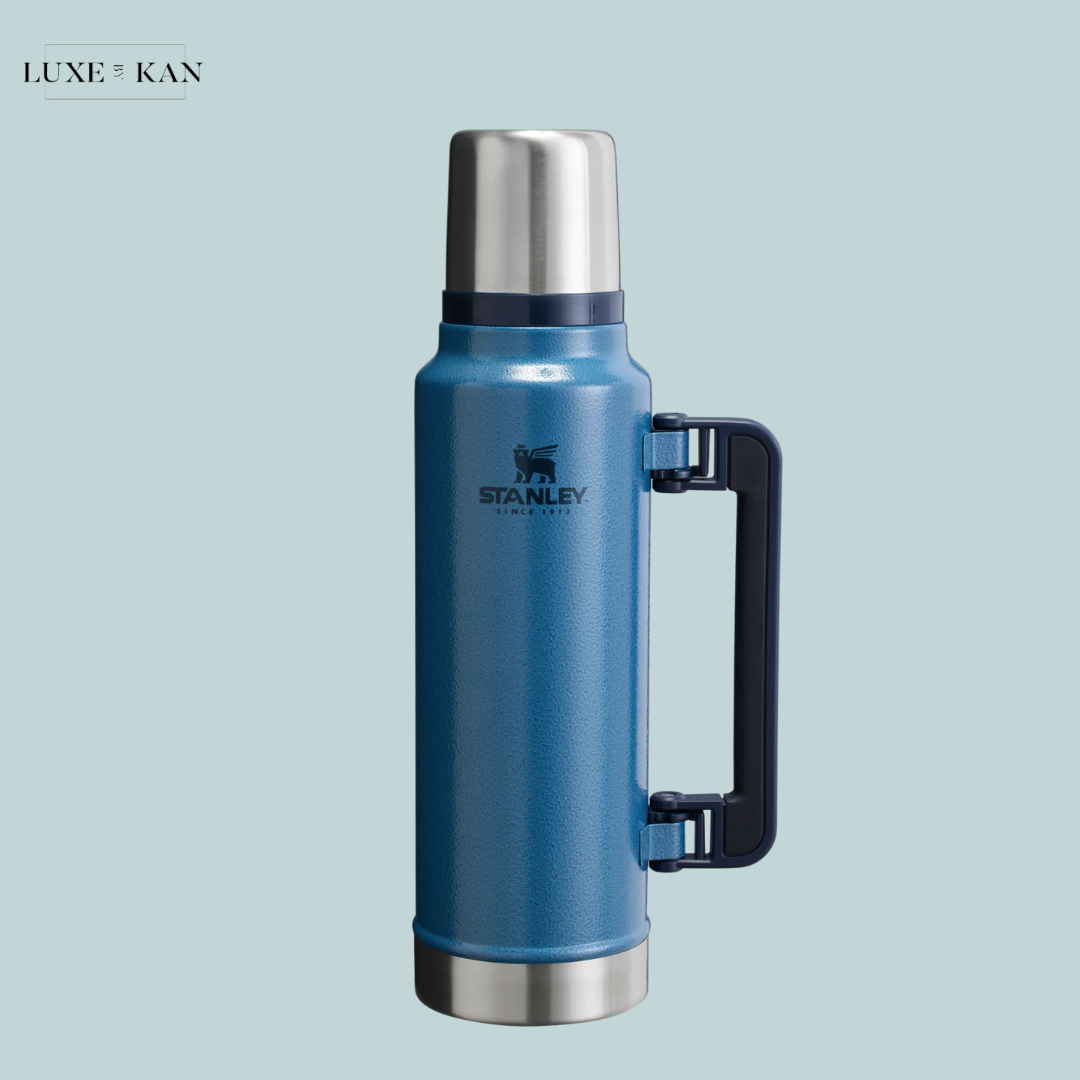 A stylish blue Stanley classic legendary bottle with a stainless steel lid and black foldable handle.