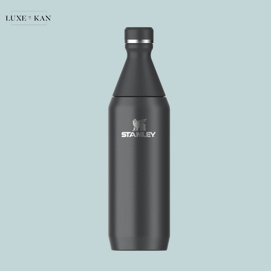 A sleek black Stanley water bottle with a silver logo, set against a light blue background. Stylish and functional design.