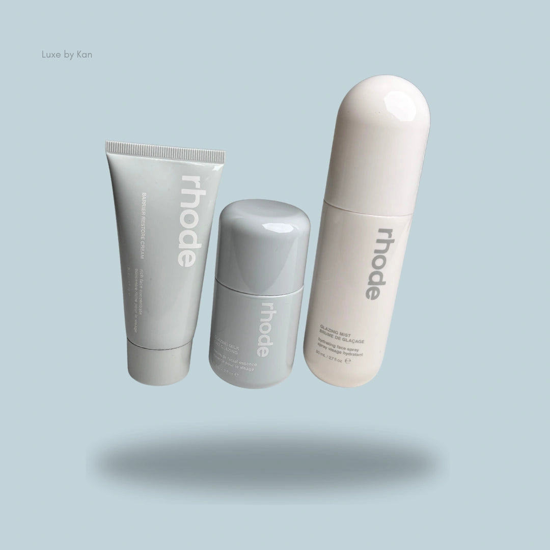 Three Rhode The Glow Set products: Barrier Restore Cream tube, Glazing Milk bottle, and Glazing Mist spray on blue background.