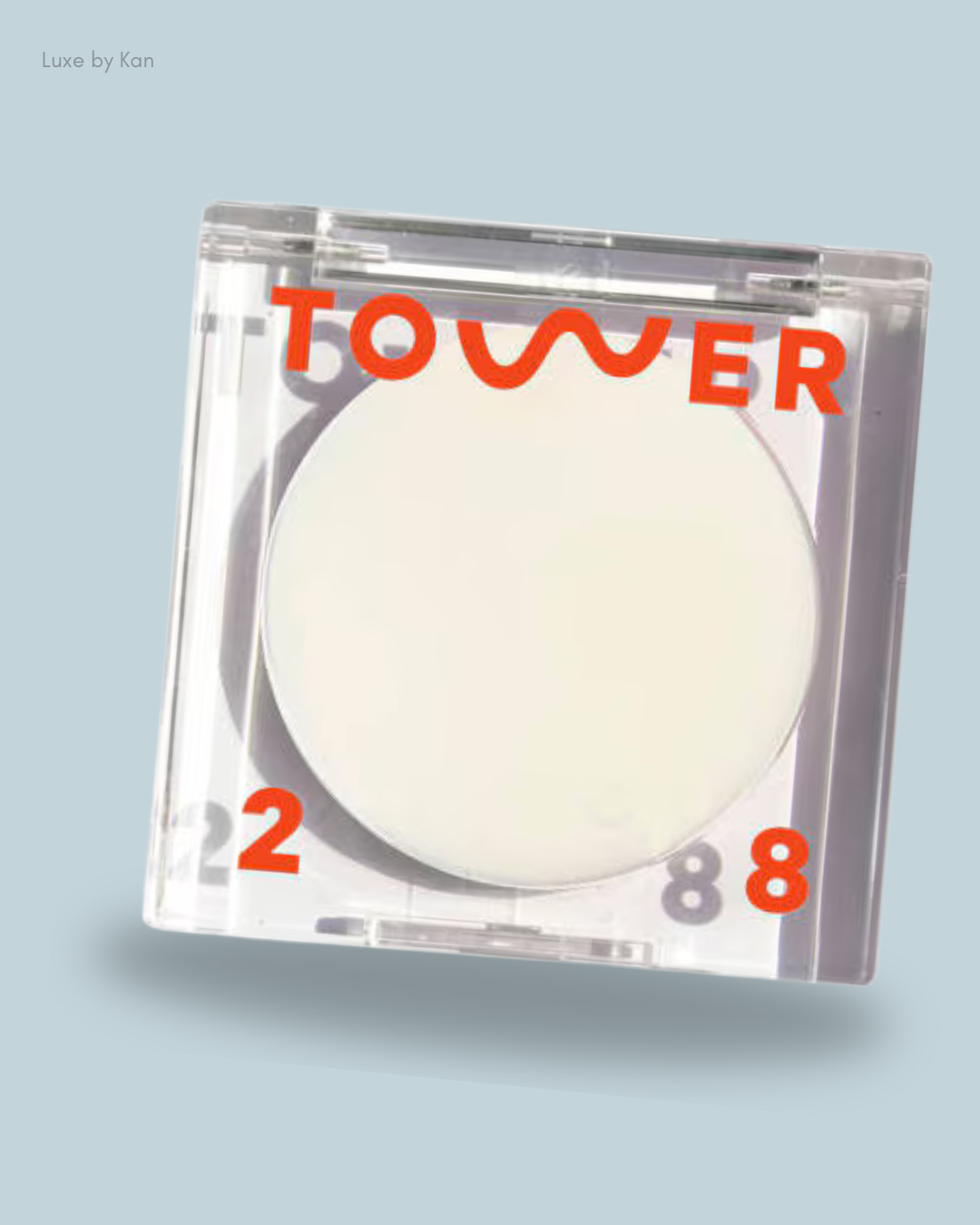 A clear compact of Tower28 SuperDew Highlighter Balm features a round white product inside, accented with bold orange lettering.