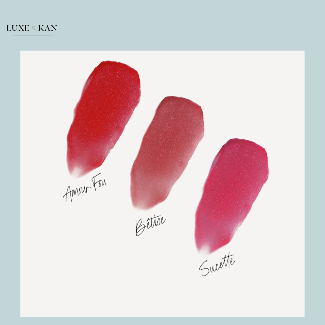 Three vibrant lipstick swatches: a bold red "Amour Fou," a soft rosy pink "Bettie," and a bright fuchsia "Sucette" on a white background.