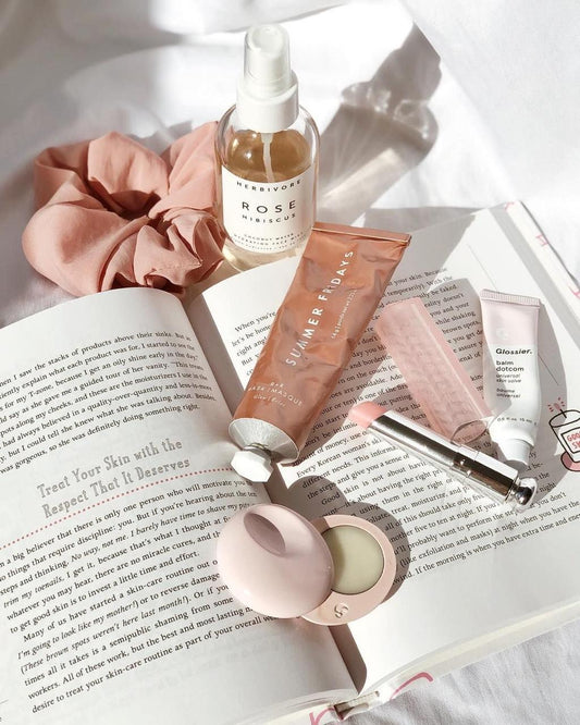 Treat yourself this Anti-Valentine’s Day with beauty self-care essentials under ₹4,999, including a Summer Fridays mask and Glossier balm, displayed across an open book in bright sunlight.