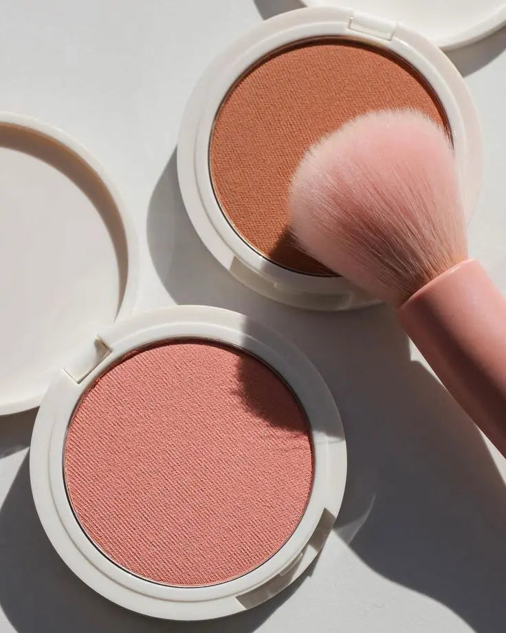 Five Chanel blushes in small clear jars with black interlocking-C logo lids, surrounded by swirls of pink, coral, and red colors.
