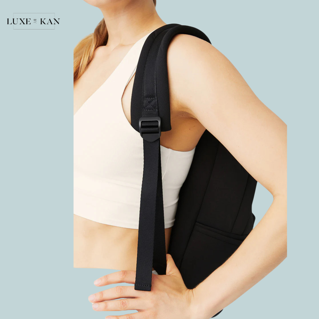 Close-up of a woman's shoulder showcasing a sleek black bag strap, worn over a light-colored outfit.