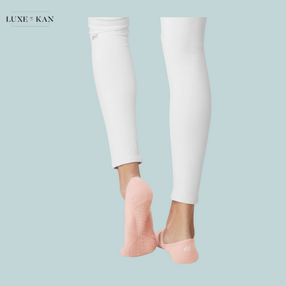 Feet wearing pink backless socks, styled with white leggings, against a soft blue background. Elegant and casual look for activewear.