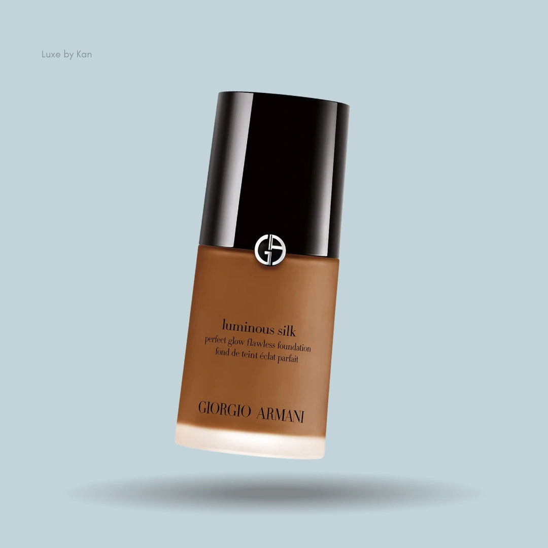 Giorgio Armani Luminous Silk foundation bottle with transparent base, brown fluid, and black cap against a light blue background.