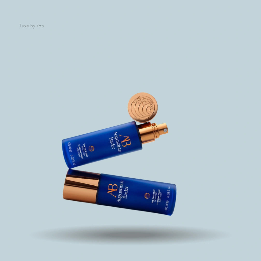 Two blue Augustinus Bader face mist bottles with gold accents.