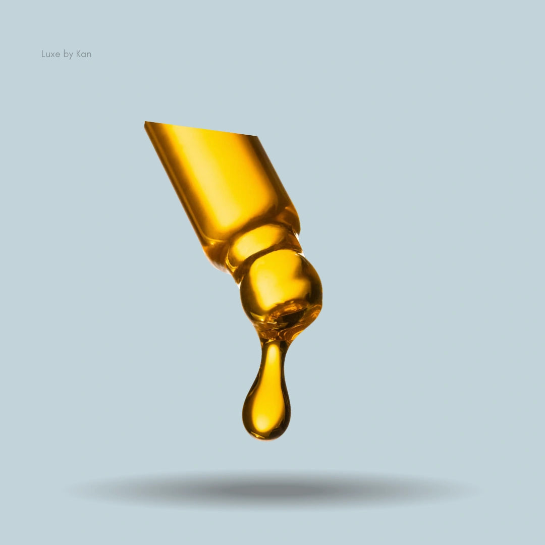 Close-up of Augustinus Bader The Face Oil dropper filled with golden oil, with a single drop suspended at the tip.