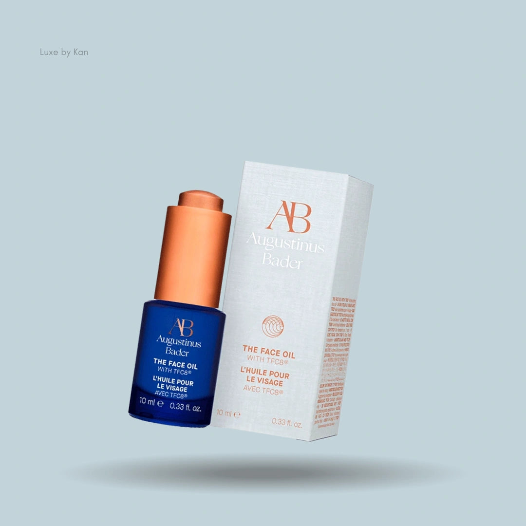 Augustinus Bader The Face Oil in blue glass bottle with orange dropper, next to product packaging.