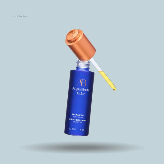 A blue bottle of Augustinus Bader Hair Oil with TFC8, featuring a gold cap and dropper.
