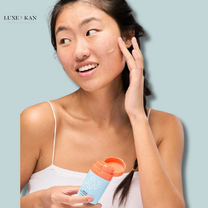 A woman holds a Bubble level up balancing gel moisturiser in her hand, while lightly touching her face against a soft blue background.