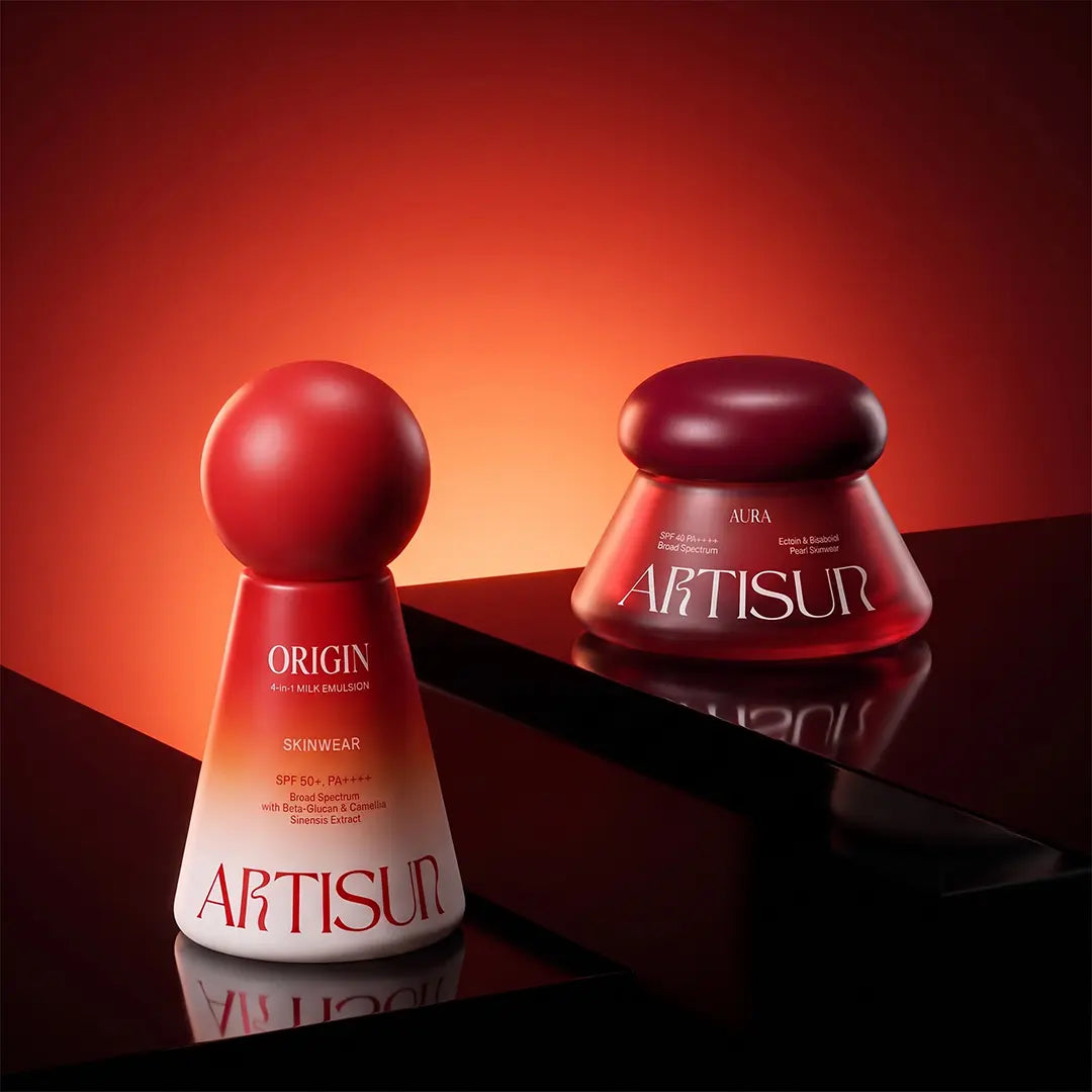 Artisun Origin 4-in-1 Milk Emulsion SPF 50+ and Aura Pearl Skinwear SPF 40 sunscreens on a red surface