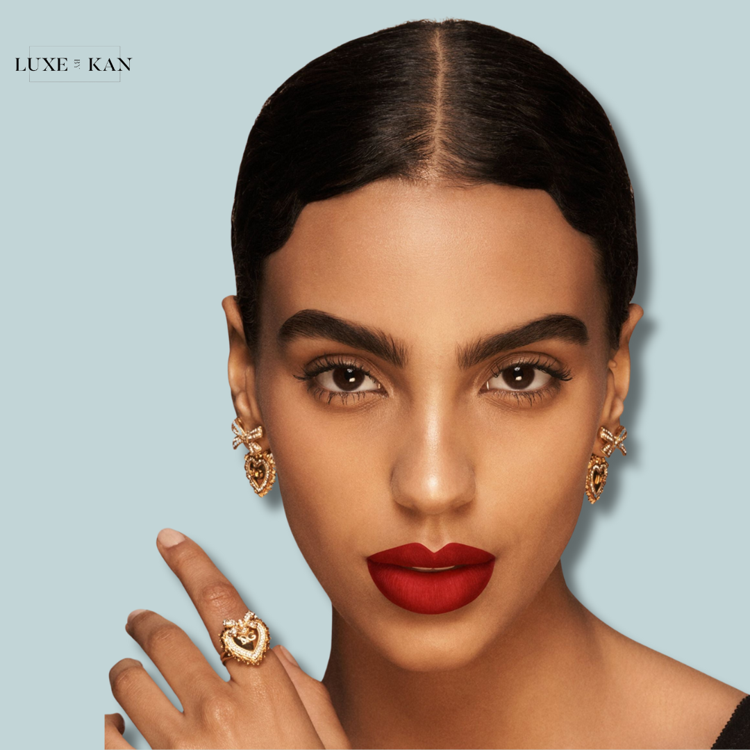 A woman with an elegant hairstyle and hand jewelry poses against a soft blue background, showcasing fashionable earrings and rings.