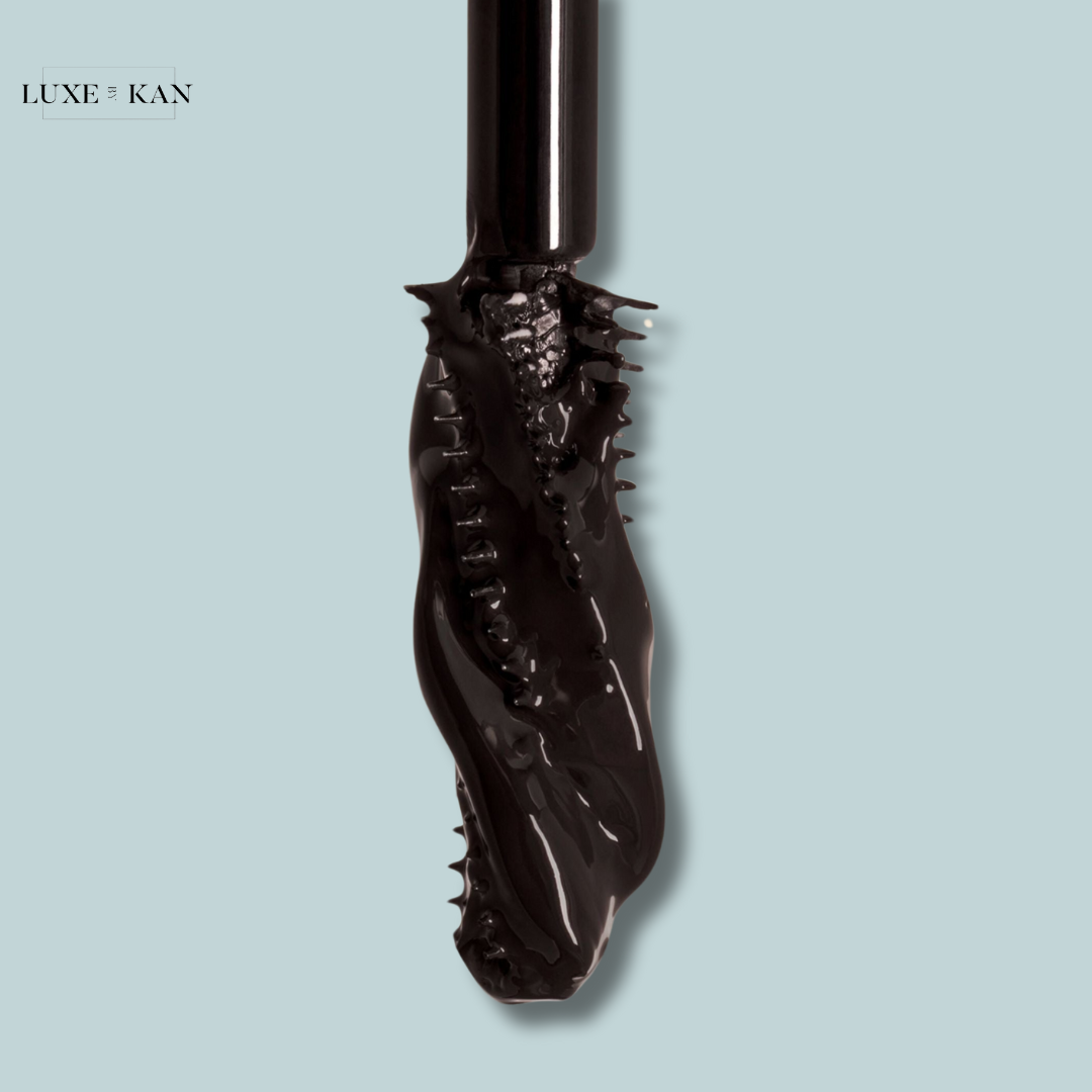 Close-up of a black mascara wand coated with thick, glossy mascara against a soft blue background. Luxe & Kan branding in the corner.