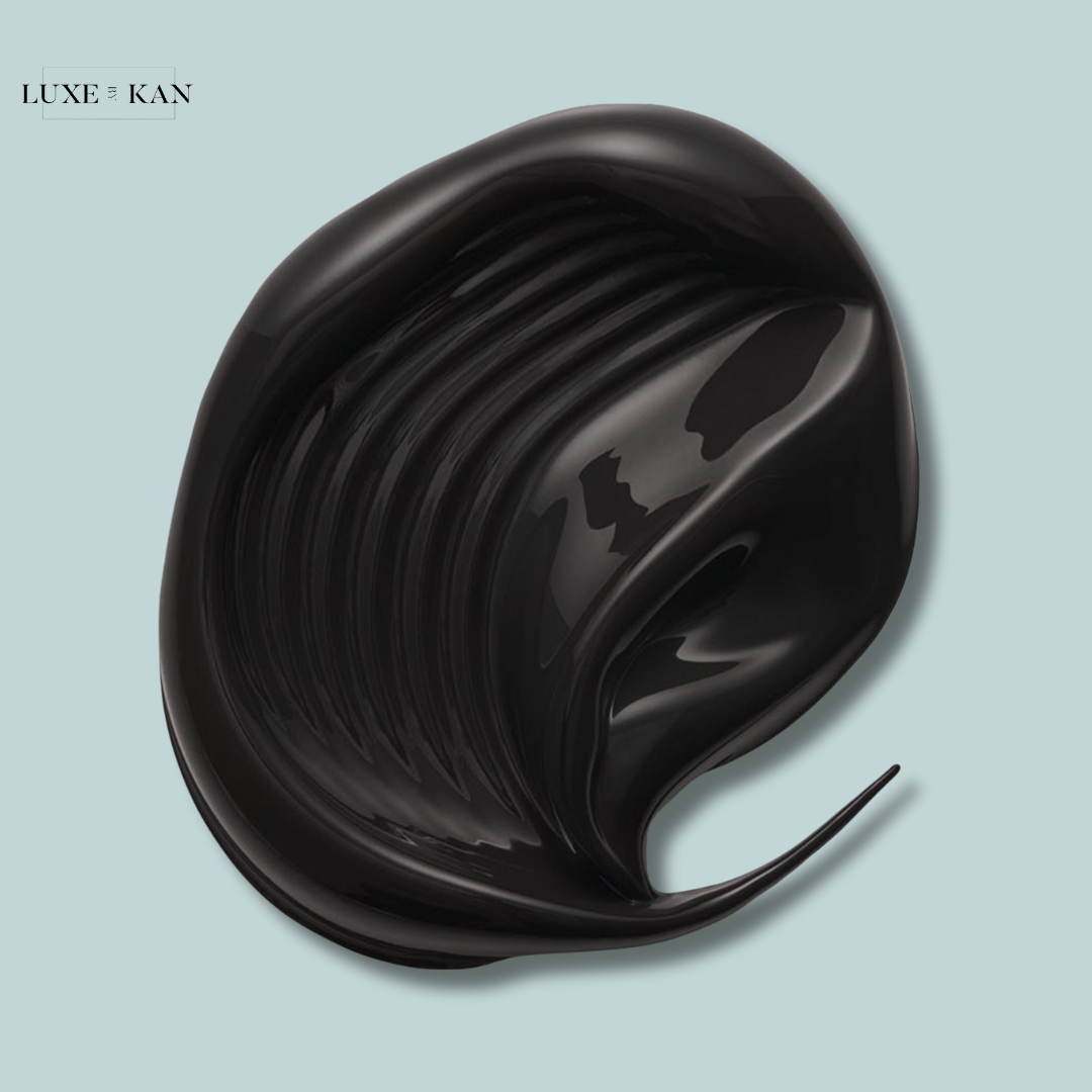 A glossy, black cosmetic product swirled on a light blue background, showcasing its smooth texture and shiny finish.