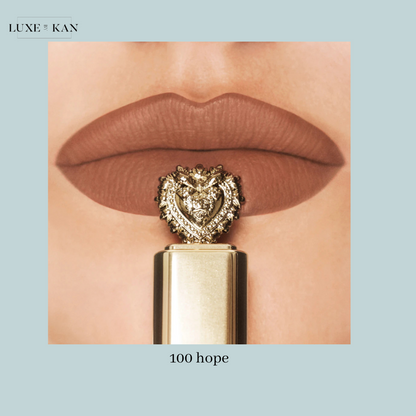 Close-up of matte brown lips holding a gold lipstick tube topped with a heart-shaped embellishment, labeled "100 hope."