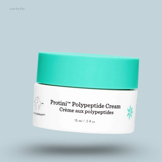 A jar of Drunk Elephant Protini Polypeptide Cream with a teal cap floats over a shadow on a light blue background.