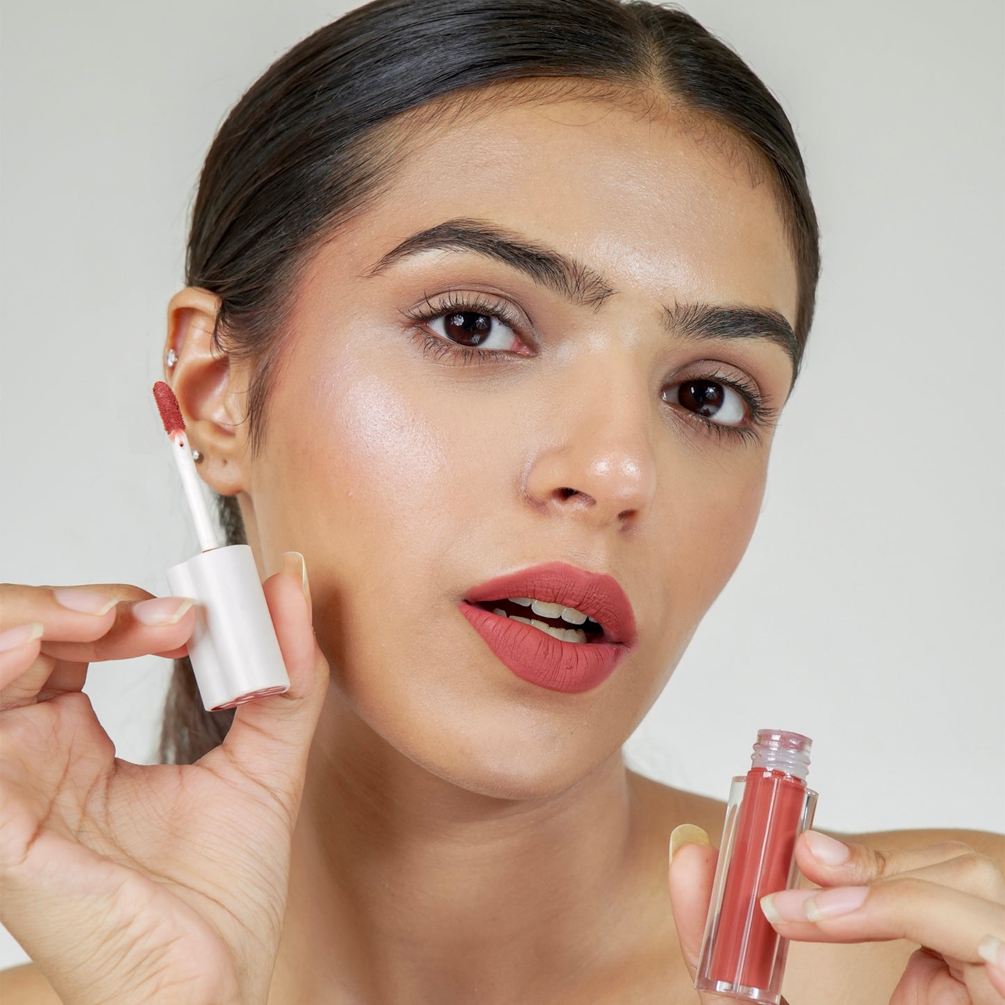 A person holds a era beauty lover girl shade wand in one hand and a small container of lip gloss in the other.