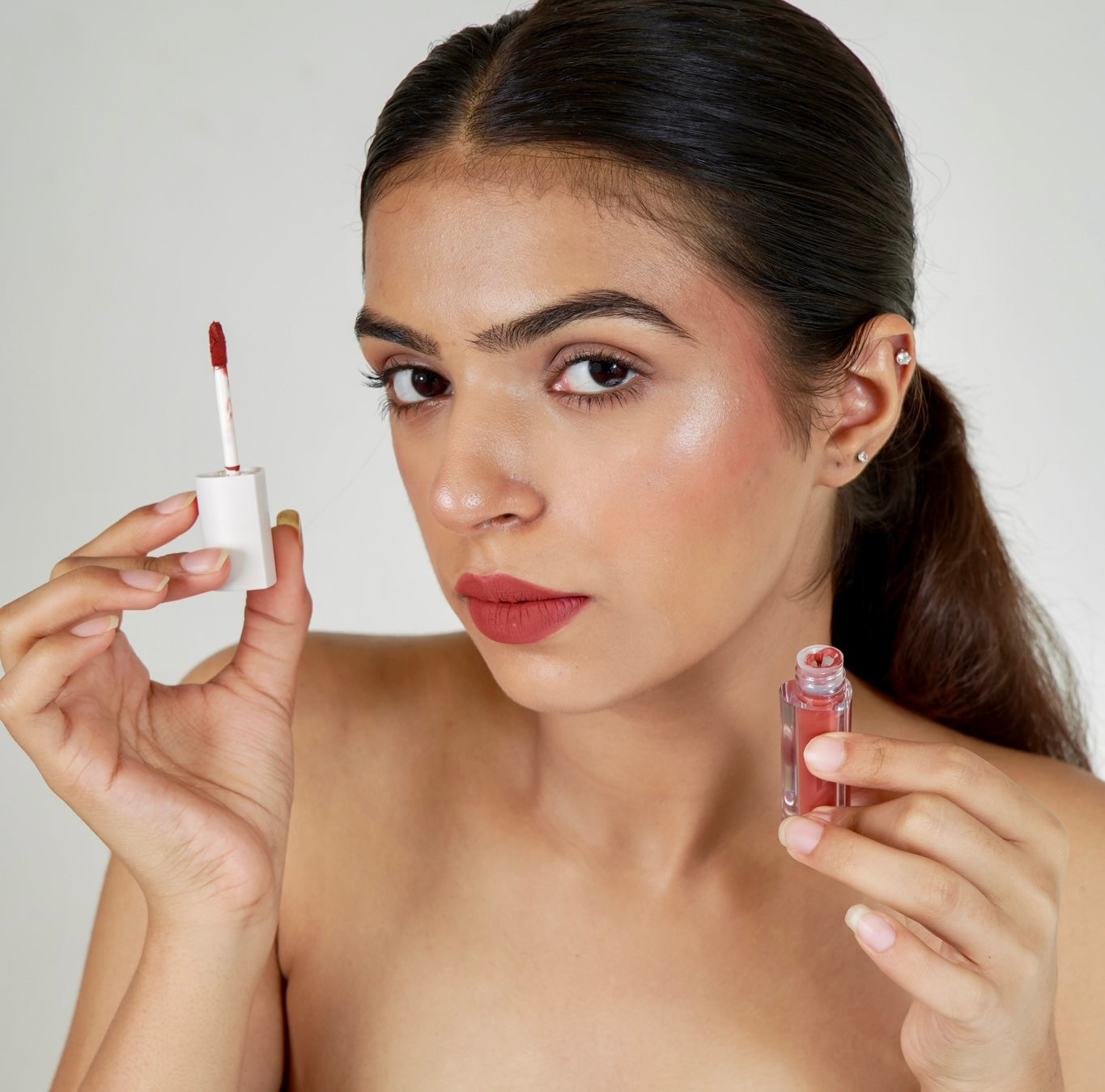 A person holds a era beauty white lip gloss applicator and a clear lip gloss bottle.