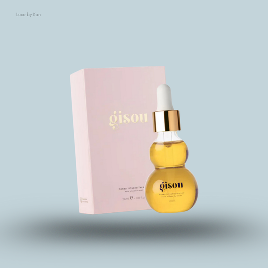 Gisou honey infused face oil in a curved glass dropper bottle next to its light pink box on a soft blue background.