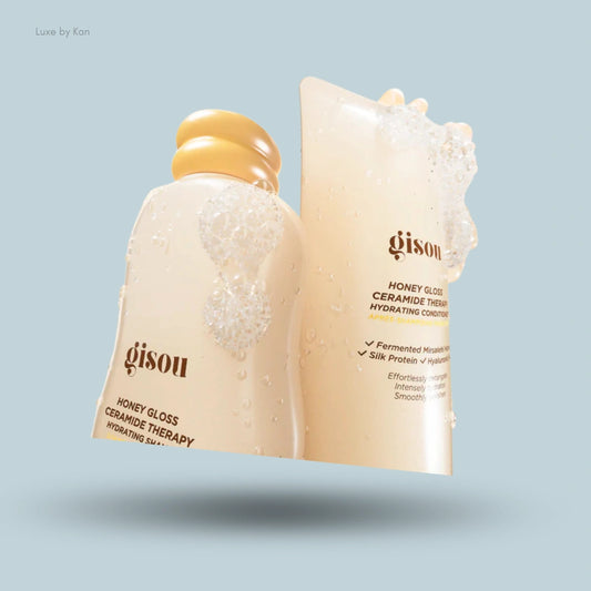 Gisou Honey Gloss hair wash duo products, surrounded by water droplets and visible soap bubbles.
