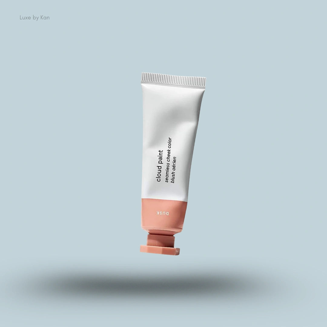 A tube of Glossier Cloud Paint Seamless Cheek Color in the shade "Dusk" floats against a light blue background.