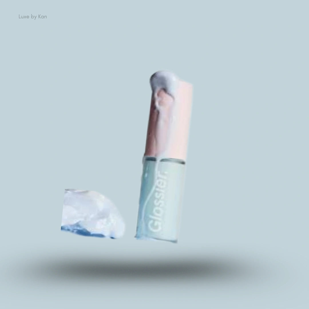 A pale blue Glossier Lip Glaze Hydrating Sheer Lip Oil tube covered partially in a white, melting substance on blue.