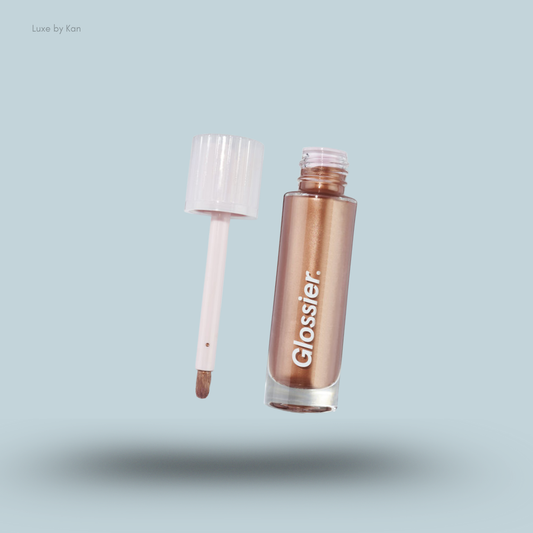 An open bottle of Glossier Skylight Liquid Highlighter in a bronze shade with the applicator wand floating next to it.