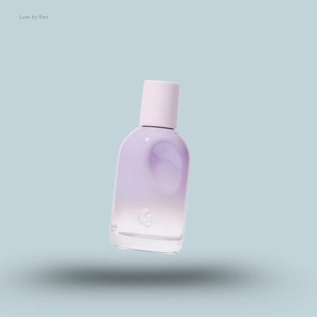 A pastel lavender and white Glossier You Fleur Perfume bottle with a light pink cap, floating on a pale blue background.