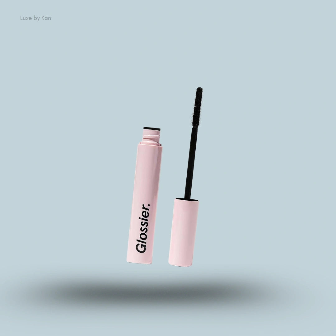An open tube of Glossier Lash Slick Lift and Lengthening Mascara with the wand floating next to it on a blue background.