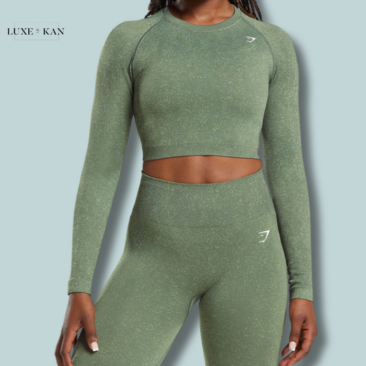 A close-up of a woman modeling an olive green Gymshark Adapt Fleck Seamless Long Sleeve Crop Top with matching leggings, showcasing a stylish and sporty workout outfit.