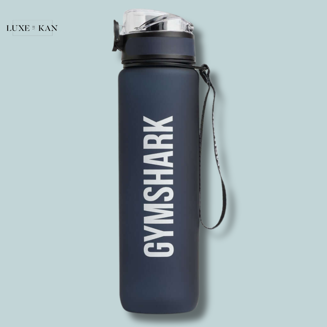 A navy blue Gymshark sports bottle with a transparent lid and a gray strap on a light blue background.