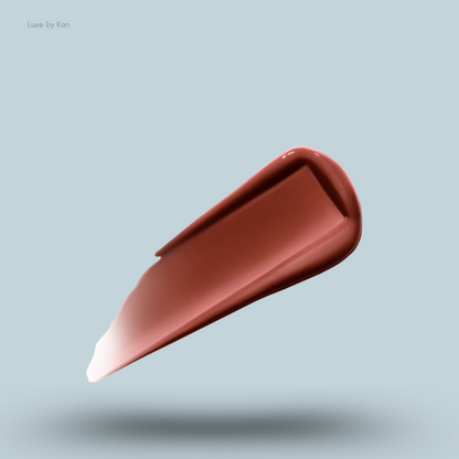 A glossy swatch of the deep rosy-brown shade 'Rouse' of the Hourglass Phantom Volumizing Glossy Lip Balm on a pale blue background.