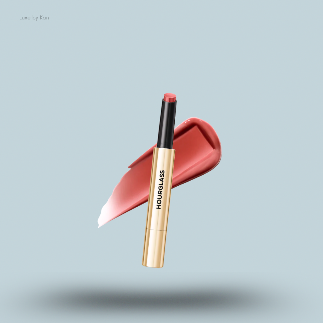 A gold and black Hourglass Phantom Volumizing Glossy Lip Balm tube is placed over a glossy pink lip product swatch.