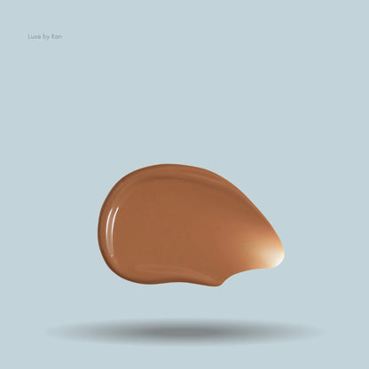 Hourglass Veil Hydrating Skin Tint swatch showing a glossy, mid-tone brown pigment against a light blue backdrop.
