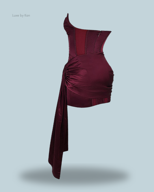 Burgundy loubella mulberry strapless corset dress featuring asymmetrical design and ruched detailing, elegantly draping to create a flowing silhouette.