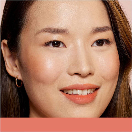 A close-up of a woman's ears, showcasing gold hoop earrings and smooth, dark hair against a soft pink background.