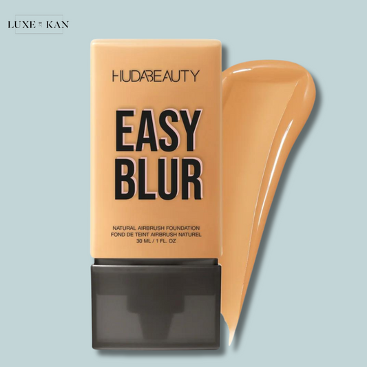 A bottle of Huda Beauty's Easy Blur foundation in a tan shade, with a flowing swatch of the foundation beside it.